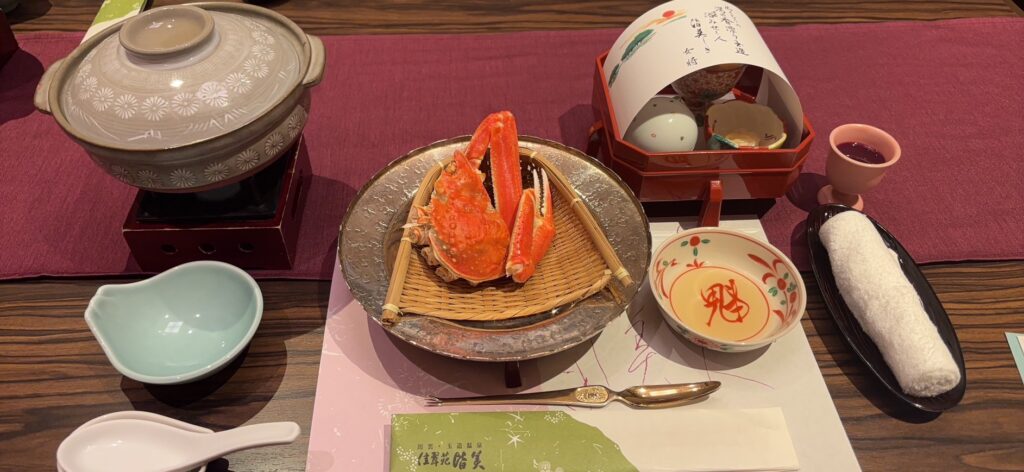 佳翠苑 皆美の夕食の会席膳。竹ざるに盛られたカニ、土鍋、小鉢などが並ぶ